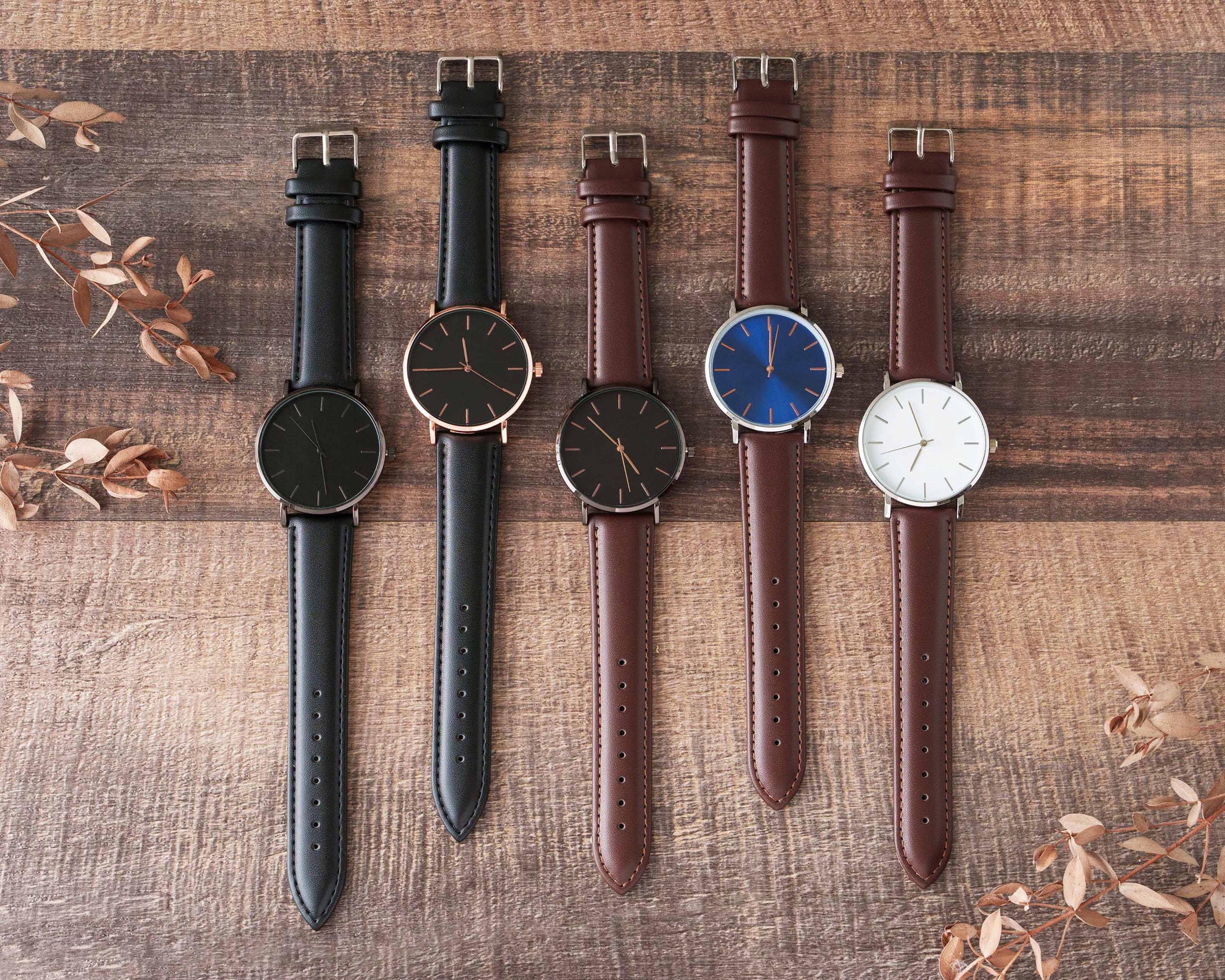 four watches are lined up on a wooden surface